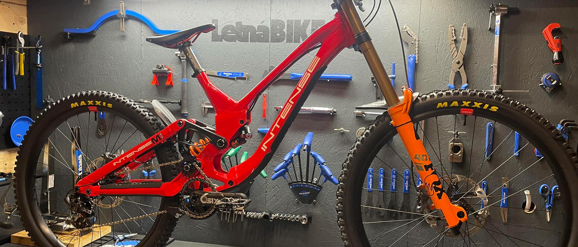 Dílna Letná Bike — celoodpružené kolo v montážním stojanu před stěnou s nářadím